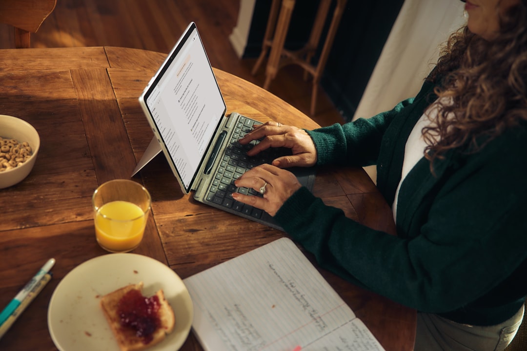 woman-typing-on-laptop-at-wooden-table-with-breakfast-ghvmdpn33vm